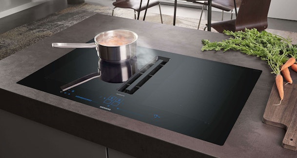 Inductie kookplaat met geïntegreerde afzuiging die stoom van een pan direct via de centrale afzuiging wegzuigt.