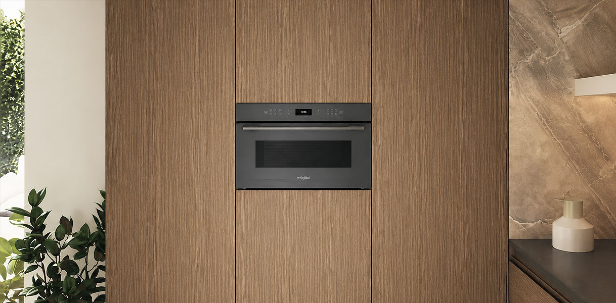 Inbouwmagnetron in een houten keukenwand tussen kastdeuren met een marmeren wand ernaast
