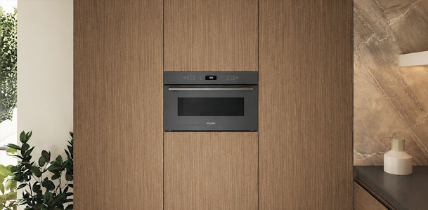 Inbouwmagnetron in een houten keukenwand tussen kastdeuren met een marmeren wand ernaast