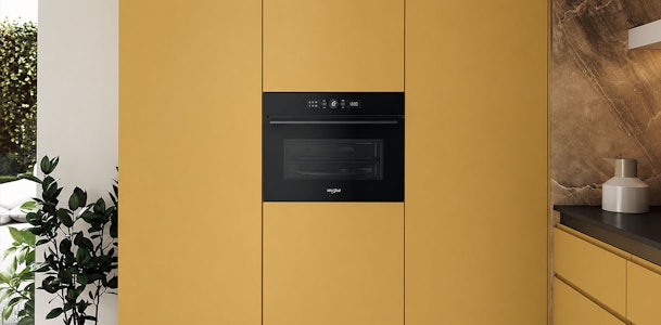 Ruimere inbouwmagnetron met display in een okerkleurige keukenwand naast een marmeren wand