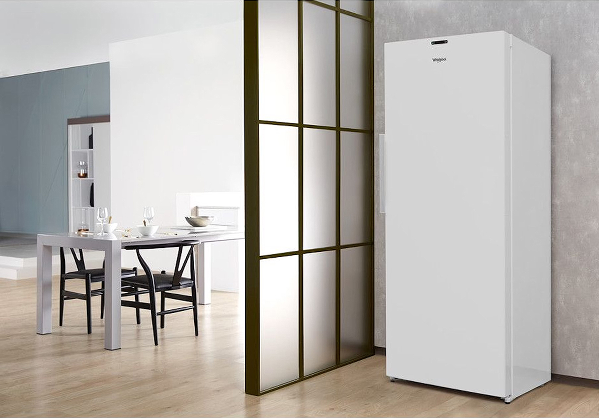 Vrijstaande Whirlpool vriezer naast een moderne eetruimte met houten vloer en glazen schuifwand