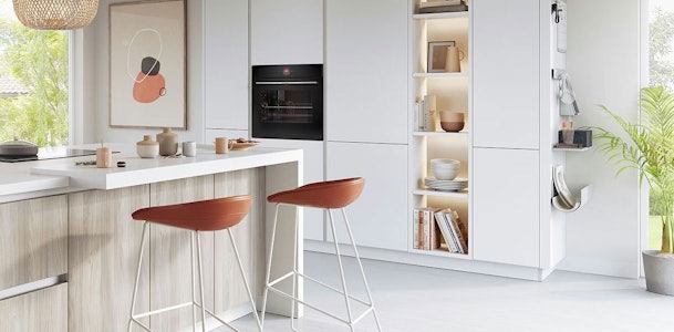 Witte keuken met greeploze fronten, eiken accenten en bruine barkrukken bij kookeiland