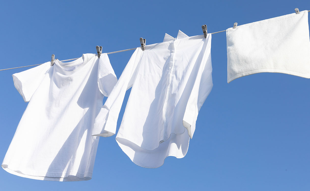 Witte was aan de waslijn: wit t-shirt, overhemd en handdoek drogen buiten tegen een strakblauwe lucht