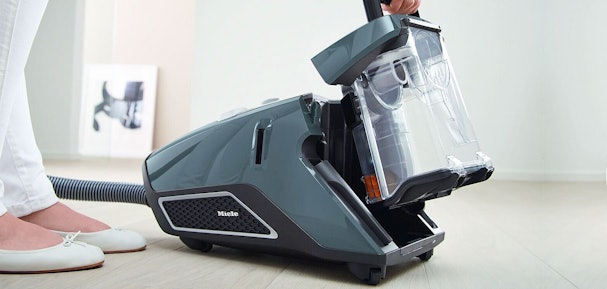Miele zakloze stofzuiger met transparant stofreservoir wordt geleegd op witte vloer