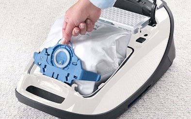 Hand plaatst nieuwe stofzuigerzak in witte sledestofzuiger voor optimale zuigkracht prestaties
