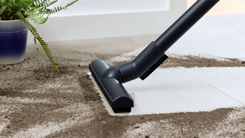 Stofzuiger mondstuk zuigt vuil en stof van tegelvloer met verschillende vloertypes zichtbaar