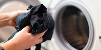 Handen stoppen zwarte kleding in een witte wasmachine