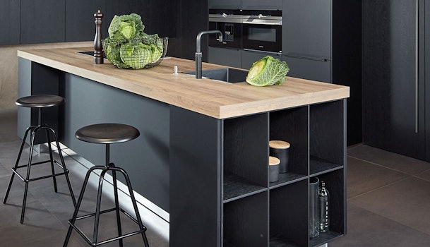 Moderne zwarte keuken met kookeiland, houten werkblad en donkere kasten voor een luxe en krachtige uitstraling.