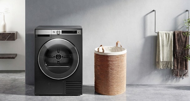 Zwarte droger in moderne wasruimte gecombineerd met betonnen muur en gevlochten wasmand